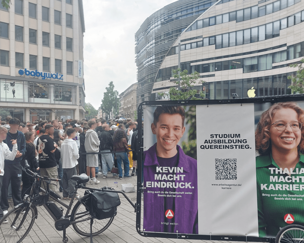 Vor der langen Schlange des Apple Stores in Düsseldorf haben die Düsseldorfer viel Zeit, die Fahrradwerbung zu beäugen. 